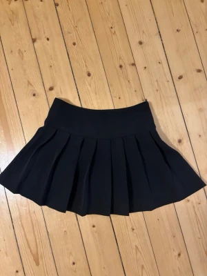 Svart plisserad kjol från Gina Tricot - Säljer en svart kortkjol från Gina Tricot med bred linning och snygga plisserade veck. Nästan oanvänd. 
