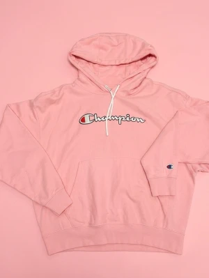 Rosa Champion hoodie med huva - Säljer en rosa hoodie från Champion med vit snörning och stor magficka. Tröjan har en oversized passform, ribbade muddar och logotypen broderad på ärmen. Som du ser är den inte struken, så ser mycket bättre ut när den är😅