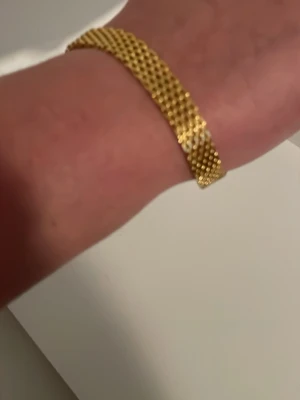 Guldpläterat armband i 18K  - Snyggt armband i 18 k guldpläterat detaljer som ger en lyxig känsla. Armbandet har ett brett band och ett smidigt klolås med bricka där det står 18K. Perfekt för dig som gillar stilrena och exklusiva accessoarer.