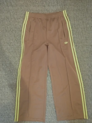 Adidas firebird loose  - Träningsbyxor i färgen cardboard signal green. Fickor med dragkedjor framtill och dragkedjor i benslut. Strl m short, 75 cm innerbenlängd.. sparsamt använda men har ändå lyckats få trådslitning på benet. 