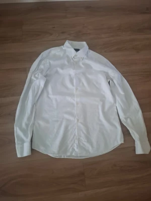 Vit klassisk skjorta med knappar - Säljer en vit skjorta med klassisk krage och knäppning framtill. Skjortan har lång ärm och är tillverkad i bomull, perfekt för en clean och stilren look. Passar till många olika outfits och är ett måste i garderoben.