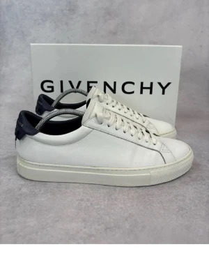 Vita Givenchy sneakers i läder - Stilrena vita sneakers från Givenchy i mjukt läder med mörkblå detalj på hälen och Givenchy-logga. Klassisk låg modell med vita snören och tjock sula. Perfekta för dig som gillar minimalistisk och lyxig design. Passar perfekt nu till sommaren! Tveka inte med att ställ frågor!