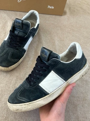 Valentino svartvita sneakers i mocka - Snygga sneakers från Valentino i svart mocka med vita detaljer och svartvita skosnören. Klassisk låg modell med vit sula och diskret logga på plösen. Perfekta för dig som gillar stilrena och exklusiva skor med en sportig touch.Går säkert att laga eller ta till skomakeri.