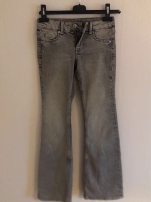 Grå bootcut jeans med slitning - Säljer ett par ljus grå bootcut jeans med snygg slitning och klassiska fickor. 