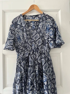 Blåvit klänning från Zara - Snygg blåvit från Zara med kort ärm. Klänningen har ett unikt mönster i blått och vitt och är tillverkad i ett lätt och luftigt material, perfekt för varmare dagar.