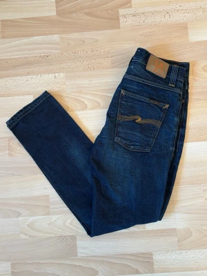 Nudie jeans  - Säljer ett par snygga mörkblå Nudie Jeans i mycket fint skick. Klassisk mörk indigo-tvätt med snygga naturliga slitningar och den ikoniska broderingen på bakfickan. Perfekta både till vardags och för en mer uppklädd look. ✅ Bra begagnat skick ✅ Inga hål eller större skador ✅ Mörk tvätt som passar till allt ✅ Kvalitetsdenim från Nudie Jeans Storlek: W32 L32 Modell: Grim Tim Nypris: ca 1600kr  Skickas snabbt och packas väl. Hör gärna av dig om du vill ha fler bilder eller mått!