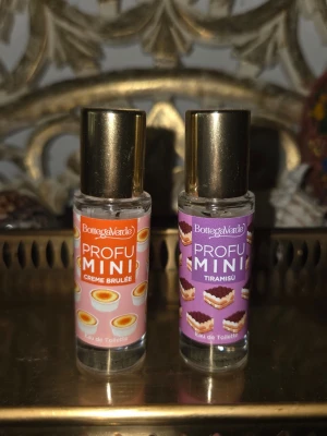 Bottega Verde Profu Mini parfymduo - Två små flaskor parfym från Bottega Verde, Profu Mini-serien. Ena doften är Creme Brulée med orange etikett och små dessertmotiv, den andra är Tiramisu med lila etikett och tårtbitar. Båda har guldfärgade lock och genomskinliga glasflaskor.