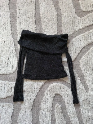 Svart glittrig offshoulder topp - Snygg svart glittrig offshoulder topp med långa, transparenta ärmar. Toppen är croppad och har en åtsittande passform som framhäver figuren. Använd ett fåtal gånger. 