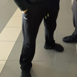 Boss byxor - Svarta mjukisbyxor från Hugo Boss med diskret logga på sidan och snörning i midjan med gula detaljer. Byxorna har en normal passform och är tillverkade i mjukt bomullsmaterial, perfekta för chill dagar. Snygg och enkel design som funkar till sneakers.