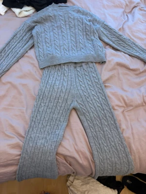 Grått kabelstickat loungewear-set - Mysigt loungewear-set i ljusgrått med kabelstickat mönster. Setet består av en långärmad tröja och matchande byxor med raka ben. Perfekt för chill dagar hemma och riktigt skönt material.