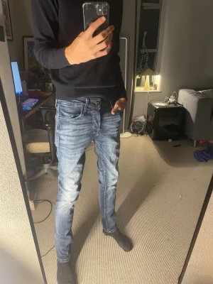 Blåa slim jeans från jack&jones - Säljer ett par blå slim fit jeans med snygga tvättade detaljer och lätt slitna partier. Jeansen har klassisk femficksdesign, normal midja och dragkedjegylf. Perfekta för dig som gillar en modern och avslappnad stil. Från jack&jones