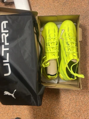 Puma Ultra gula fotbollsskor - Snygga och lätta fotbollsskor från Puma Ultra-serien i neon-gult med svarta detaljer och klassisk Puma-logga. Skorna har snörning och ovandel i syntetmaterial för bra passform och känsla på planen. Perfekta för dig som vill sticka ut på matchen! Aldrig andvända, påse och sko lådan ingår