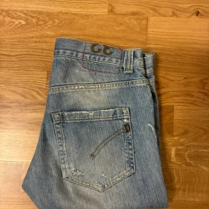 Ljusblå slitna jeans från dondup - Säljer ett par ljusblå jeans från dondup med slitningar och distressed detaljer. Klassisk femficksmodell med raka ben och låg midja. Perfekta för en avslappnad streetstil.