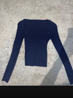 Mörkblå ribbstickad topp - Snygg mörkblå ribbstickad topp med lång ärm och fyrkantig halsringning. Tröjan är figurnära och har en modern, stilren look som passar perfekt till jeans eller kjol. Materialet är stretchigt och mjukt för en bekväm känsla.