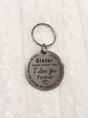 Nyckelring med text till syster - Rund silverfärgad nyckelring i metall med ingraverad text: 'Sister, never forget that I love you forever'. Perfekt som personlig accessoar eller present till din syster. Dekorativt hjärta ingraverat på framsidan.
