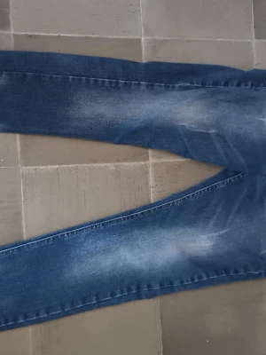 Blå Dsquared2 jeans med slitningar - Snygga blå jeans från Dsquared2 med coola slitningar och tvättade detaljer. Klassisk femficksmodell med raka ben och tydlig logotyp på bakfickan. Perfekta för en trendig och avslappnad stil.