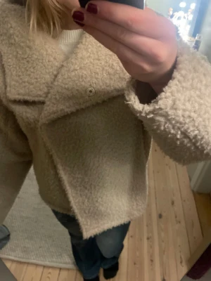 Beige teddyjacka med bred krage - Säljer en supermjuk och fluffig beige teddyjacka med bred krage och lite oversized passform. Jackan har stora slag och stängs med tryckknappar. Perfekt för dig som vill ha en mysig och trendig look i höst och vinter.