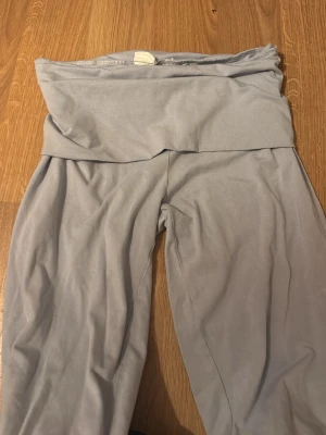 Ljusgrå loungewearbyxor Stories - Mysiga ljusgrå loungewearbyxor från Stories med bred, vikt midja och mjukt, stretchigt material. Perfekta för chill hemma eller när du vill ha det extra bekvämt. Byxorna har en avslappnad passform och är tillverkade i ett tunt tyg.