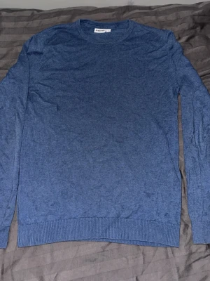 Blå tunn stickad tröja från Kappahl - En enkel och stilren blå stickad tröja från Kappahl. Tröjan har rund halsringning, långa ärmar och ribbade muddar vid ärmslut och nederkant. Perfekt att matcha med jeans eller kjol för en clean look.