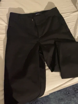 Svarta kostymbyxor Gina Tricot - Snygga svarta kostymbyxor från Gina Tricot med klassisk rak passform och hällor för skärp. Byxorna har dragkedja och knapp framtill och är gjorda i ett mjukt, vävt material som känns bekvämt hela dagen.