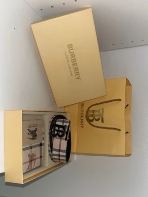 Burberry plånbok med klassiskt rutmönster - Säljer en snygg Burberry plånbok i beige med det ikoniska rutmönstret och svart detaljer. Plånboken har ett stort B-spänne och Burberrys logga tryckt på framsidan. Kommer i originalförpackning och med tillhörande påse.