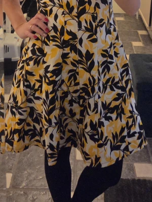 Gul och svart blommig klänning - Säljer en fantastisk ärmlös klänning med blommigt mönster i gult, svart och vitt. Klänningen har en utställd passform och rundad halsringning. Härligt material. Perfekt för dig som vill ha en färgglad och somrig look!