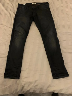 Mörkblå slim fit jeans - Snygga mörkblå slim fit jeans med klassisk femficksdesign och diskreta slitningar på låren. Jeansen har normal midja och raka ben, perfekta för en stilren och modern look. Materialet är denim med en lätt stretch för extra komfort.