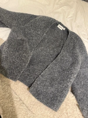 Grå stickad tröja i ull - Mysig grå stickad tröja med lång ärm och enkel design. Tröjan är tillverkad i ett tjockt, ulligt material som håller dig varm under kyliga dagar. Perfekt för lager-på-lager och har en klassisk passform.