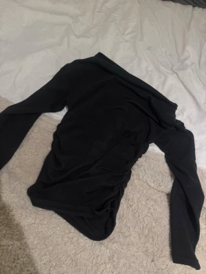 Svart offshoulder topp - Snygg svart offshoulder topp med långa ärmar. Perfekt för dig som vill ha en stilren och trendig look. Toppens material känns mjukt och stretchigt, vilket gör den bekväm att bära. Passar till många olika outfits och är enkel att matcha.