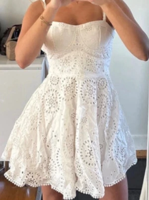 Zara sommarklänning - Söt vit klänning med broderade detaljer och utställt kjolparti. Klänningen har smala axelband och markerad byst med sömmar. Perfekt för varma dagar, avslutningar och student. Banden är insydda men kan spretas upp. Använd en gång köptes för 700kr