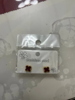 Blommiga örhängen i rostfritt stål - Säljer ett par små örhängen i form av blommor med vinröd färg och guldkant. Tillverkade i rostfritt stål, perfekta för dig som vill ha något enkelt men ändå snyggt. Levereras i originalförpackning.