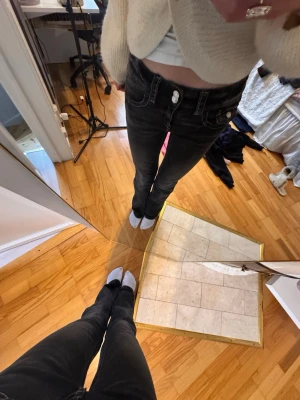 Svarta utsvängda jeans med kontrastsömmar - Säljer ett par svarta jeans med raka ben och vita kontrastsömmar. Jeansen har klassisk femficksdesign och silverfärgad knapp. Snygg passform som sitter tajt över höfterna och låren. Perfekta till en avslappnad vardagsstil.