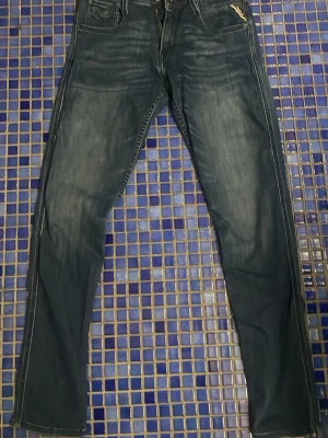 Mörkblå slim fit jeans från Replay - Säljer mina mörkblå jeans från Replay anbass slim fit-modell med klassiska fem fickor och detaljer då de är för små. Dom har använts max 2 gånger. Jeansen har en tvättad look och kontrastsömmar, perfekta för en trendig och avslappnad stil. Tillverkade i bomull med en liten stretch för extra komfort.