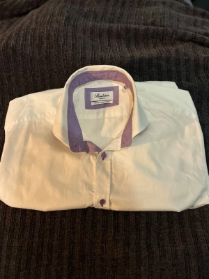 Vit skjorta Stenströms  - Klassisk vit skjorta från Stenströms med unika lila  detaljer på insidan av kragen och lila knappar. Tillverkad i tvåfaldig super bomull för en mjuk och lyxig känsla. Perfekt under en stickad tröja eller kavaj. Storlek 39, passar medium. Toppen skick! 🔥