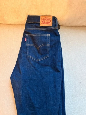Mörkblå Levi's jeans med klassisk passform - Snygga mörkblå jeans från Levi's med klassisk femficksmodell och raka ben. Jeansen har tydliga kontrastsömmar och den ikoniska läderpatchen bak i midjan. Perfekta för dig som gillar tidlös denimstil.