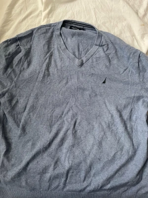 Grå stickad tröja från Nautica - Snygg grå stickad tröja från Nautica med v-ringning och diskret logga broderad på bröstet. Tröjan har ribbstickade muddar vid ärmslut och nederkant. Perfekt för lager-på-lager och enkel att matcha med jeans eller chinos.