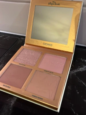 Catrice Jungle Book Face Palette - Snygg ansiktspalett från Catrice x Disney Jungle Book med fyra olika nyanser: skimrande rosa, matt ljusrosa, varm brun och beige. Paletten har spegel och guldiga detaljer, perfekt för contour, blush och highlight.