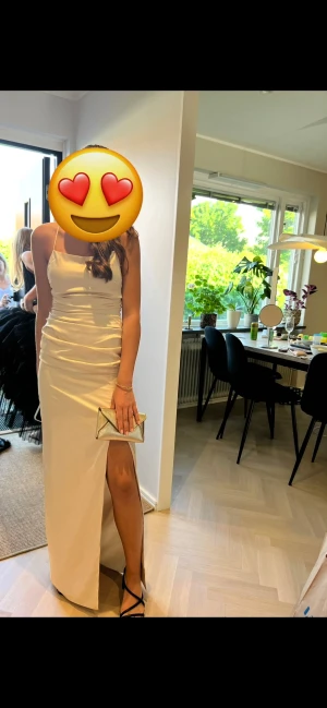 Så fin Champagnefärgad långklänning Bubbleroom - Supersnygg långklänning från Bubbleroom i champagnefärgat satinliknande material. Klänningen har figurnära passform, draperade detaljer i midjan och en hög slits framtill. Perfekt för dig som vill sticka ut med en elegant look.