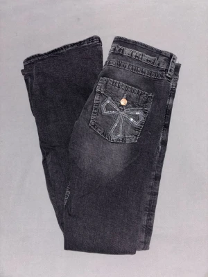 Low waist bootcut jeans - Snygga svarta low waist bootcut jeans med coolt broderi på bakfickan och knappdetalj. Jeansen har en lätt tvättad look och klassisk femficksdesign. Perfekta för dig som gillar en avslappnad men trendig stil❤️Knapparna bak på byxan är fejk. Det går alltså att använda bakfickorna utan att knäppa upp knappen! Måttet rätt över midjan är ca 35cm och innerbenslängden är ca 78cm. Säljer dessa eftersom de inte kommer till användning längre, de är bara använda fåtal gånger. Skriv gärna innan ni köper❤️