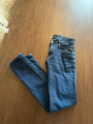 Blå Replay jeans - Snygga blå slim jeans från Replay med dragkedjedetalj vid fickan och klassiska kontrastsömmar. Använda 2 gånger tidigare. Jeansen har fem fickor, normal midja och är gjorda i stretchigt denim för extra komfort. Perfekta för en avslappnad och trendig look.