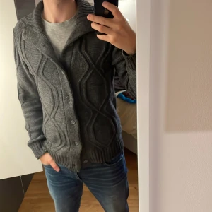 Grå stickad kofta i ull - Säljer en snygg grå stickad kofta  Den har ett coolt kabelstickat mönster och knappar framtill. Perfekt för höst och vinter, och den är supermysig att ha på sig. Passar både till vardags och lite finare tillfällen. Sjukt fet. ” Passar om man bär M också 