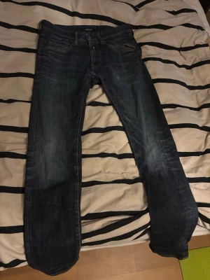 Mörkblå raka jeans från Replay - Säljer ett par mörkblå jeans från LEVI'S med raka ben och klassisk femficksmodell. Jeansen har snygga slitningar och kontrastsömmar, samt detaljerade bakfickor med broderi. Perfekta för en avslappnad och trendig stil.