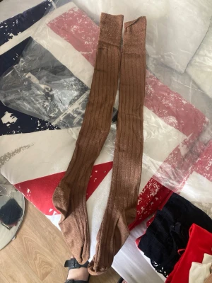 Bruna ribbade knästrumpor - Säljer ett par långa bruna knästrumpor med ribbad struktur. Perfekta att styla till kjol eller shorts för en trendig look. Strumporna är mjuka och stretchiga, vilket gör dem bekväma hela dagen.