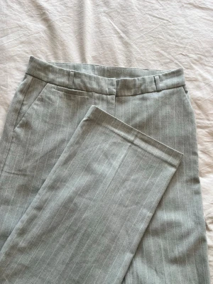 Grå kostymbyxor med smala ränder - Snygga grå kostymbyxor med tunna vita kritstrecksränder. Med raka ben 