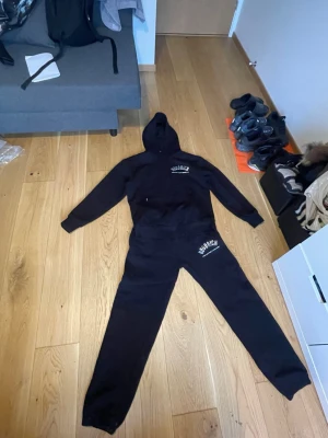 Svart Hoodrich loungewear set - Säljer ett svart loungewear set från Hoodrich med matchande hoodie och byxor. Hoodien har tryck med 'Hoodrich' på bröstet och ryggen samt texten 'From Nothing To Something'. Byxorna har samma logga på ena benet. Perfekt för chill dagar hemma.