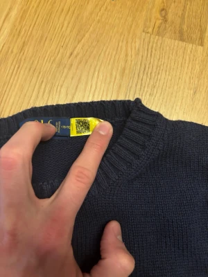 Mörkblå stickad tröja Polo Ralph Lauren - Mörkblå stickad tröja från Polo Ralph Lauren med rund halsringning och ribbade muddar vid ärmslut och nederkant. Klassisk broderad logga på bröstet. Perfekt till höst och vinter för en stilren look. Storlek S. Hör gärna av om pris