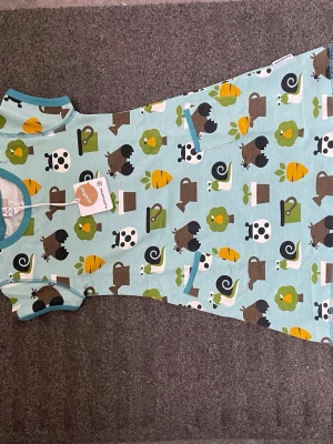 Blå kort klänning med djurmönster - Kortärmad blå klänning från DUNS Sweden med lekfullt mönster av djur, sniglar, träd och vattenkannor i grönt, brunt, vitt och gult. Tillverkad i mjuk bomull med rund hals och kontrasterande kantband. Perfekt för dig som gillar färgglada prints!