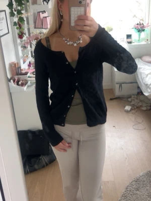 Svart cardigan med knappar - Snygg svart cardigan med knäppning framtill och långa ärmar. Tröjan har en smal passform och är tillverkad i ett mjukt, tunt material som passar perfekt till lager på lager. Enkel och stilren design som funkar till det mesta.