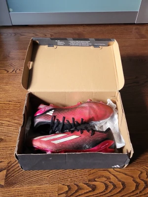 Adidas röda och svarta fotbollsskor - Säljer ett par snygga fotbollsskor från Adidas i rött och svart med vita detaljer. Skorna har låg profil, snörning och är tillverkade i syntetmaterial för bra grepp och känsla på planen. Perfekta för dig som vill sticka ut på matchen! De kostade dryga 2 000 när jag köpte. Priset är inte hugget i sten.