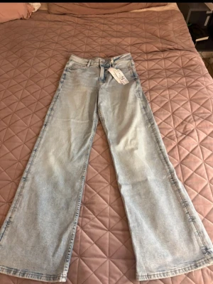 Ljusa wide leg jeans från Lindex - Säljer ett par ljusblå wide leg jeans från Gina Tricot i storlek 36. Jeansen har hög midja, klassisk femficksmodell och raka, vida ben. Tillverkade i bomull med en skön och avslappnad passform. Perfekta för en trendig och bekväm look.